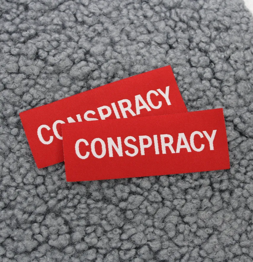 Нашивка жаккардова "CONSPIRACY" 80*30 мм червоного кольору на флізеліновій основі-1