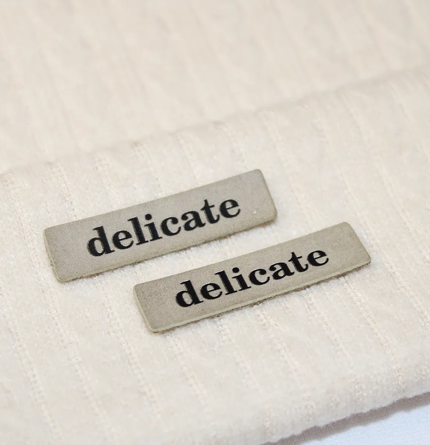 Нашивка "Delicate" 40*10 мм бежевого цвета с черной надписью.-1
